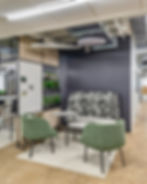 Modern open-office environment at COFCO, a Henricksen Company Philadelphia showroom, featuring collaborative workstations with red and wood finishes, lounge seating, glass-enclosed meeting rooms, and natural light highlighting the downtown skyline views